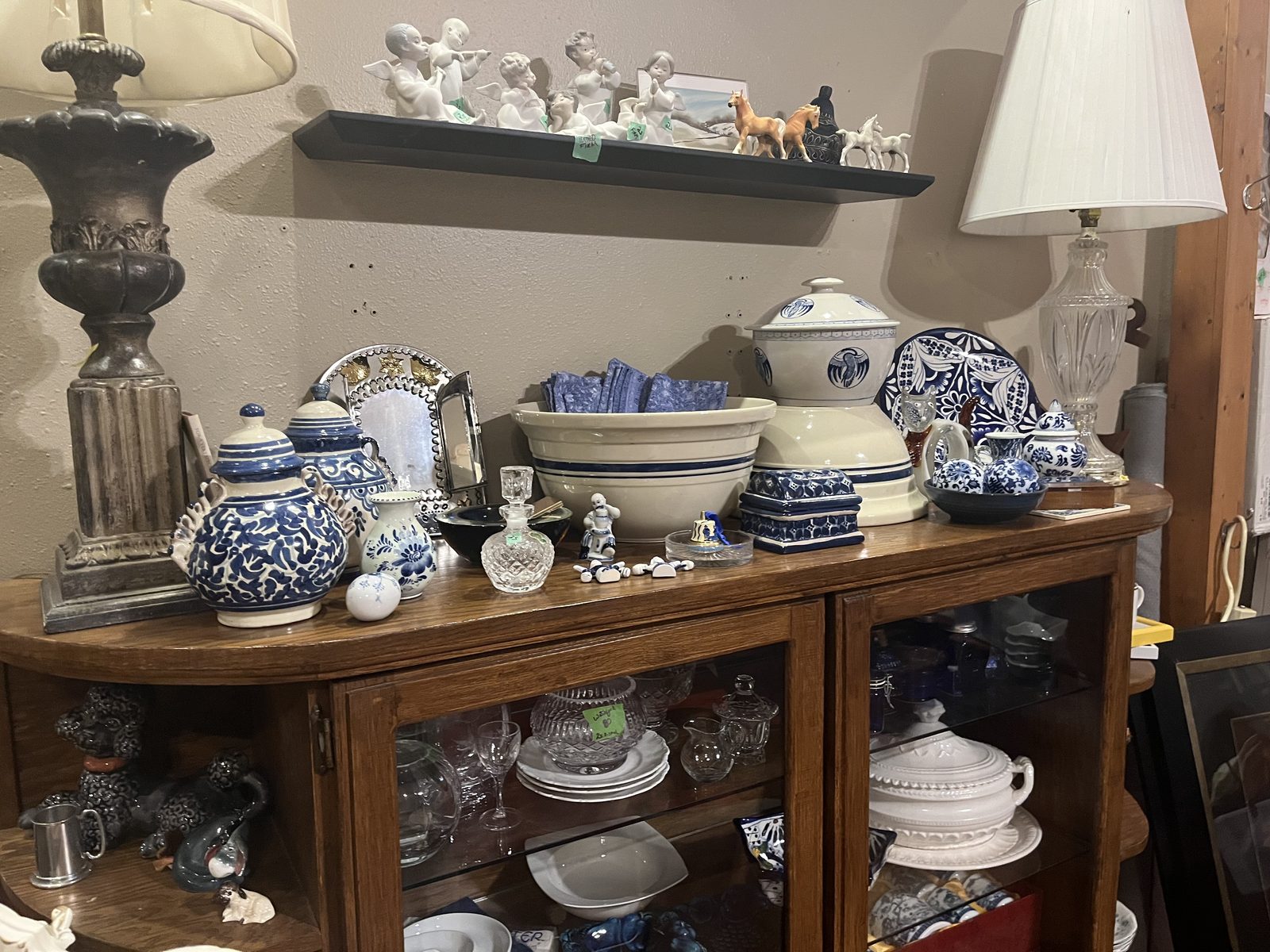 Blue and white pottery, a stoneware mixing bowl, a lidded tureen and cut glass on top of an oak china cabinet, figurines on the shelf above